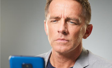Man Squinting While Looking at Blue Phone